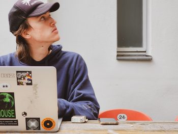 young man sitting on computer with a ball cap