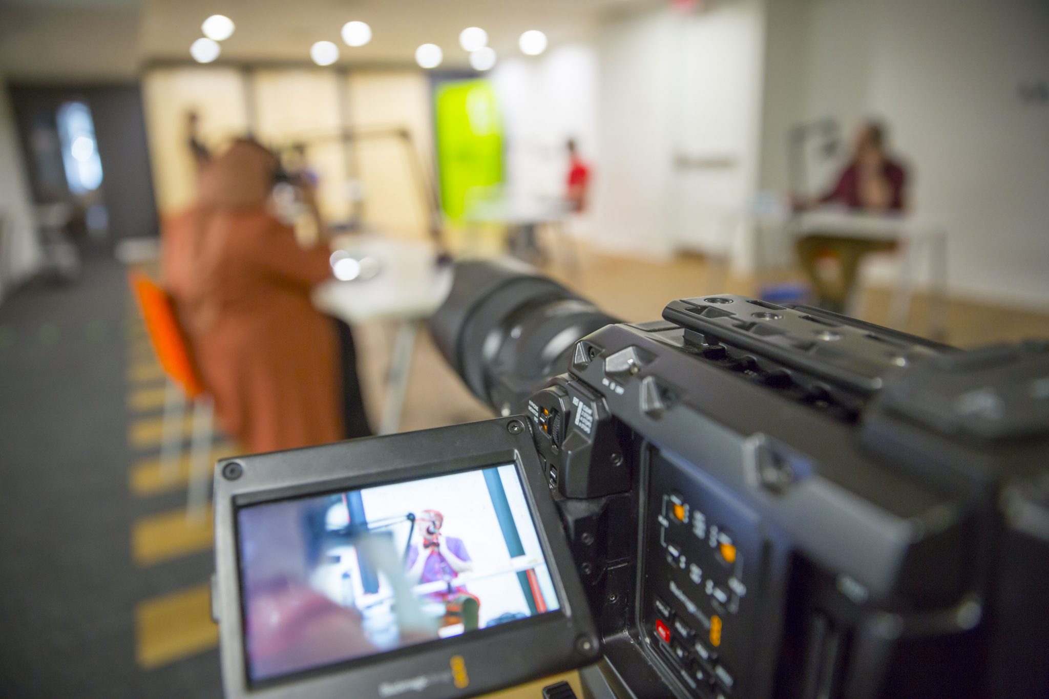 view of recording of The Computer is Your Recorded through the monitor on a video camera. Players also have microphones at socially distanced tables which suggests abstraction, distance, and the mediation of technology